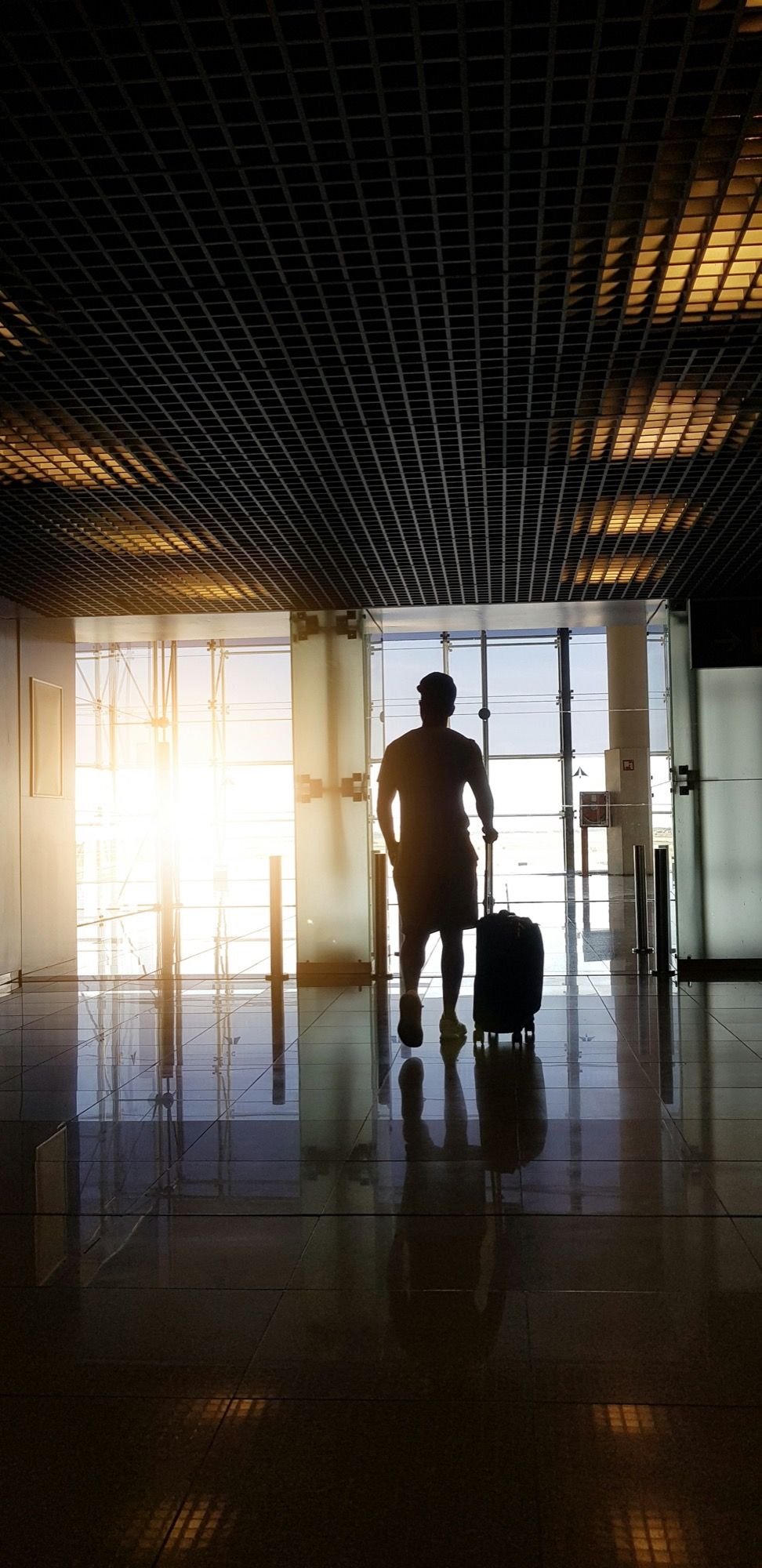 A traveller with a suitcase in silhouette against the windows of Barcelona airport