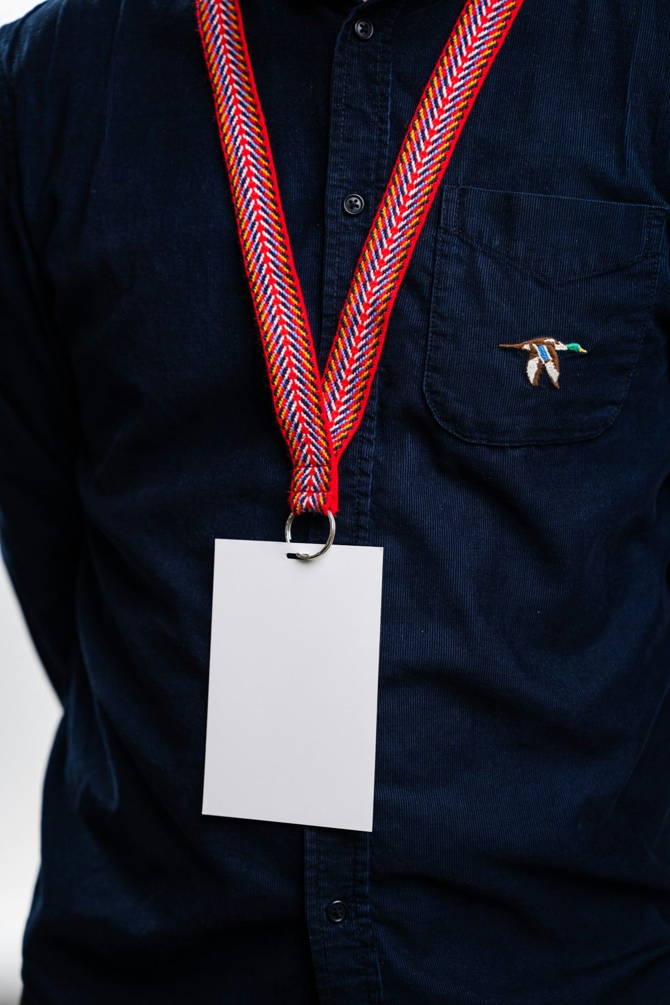 A blank event badge on a red patterned lanyard over a navy shirt