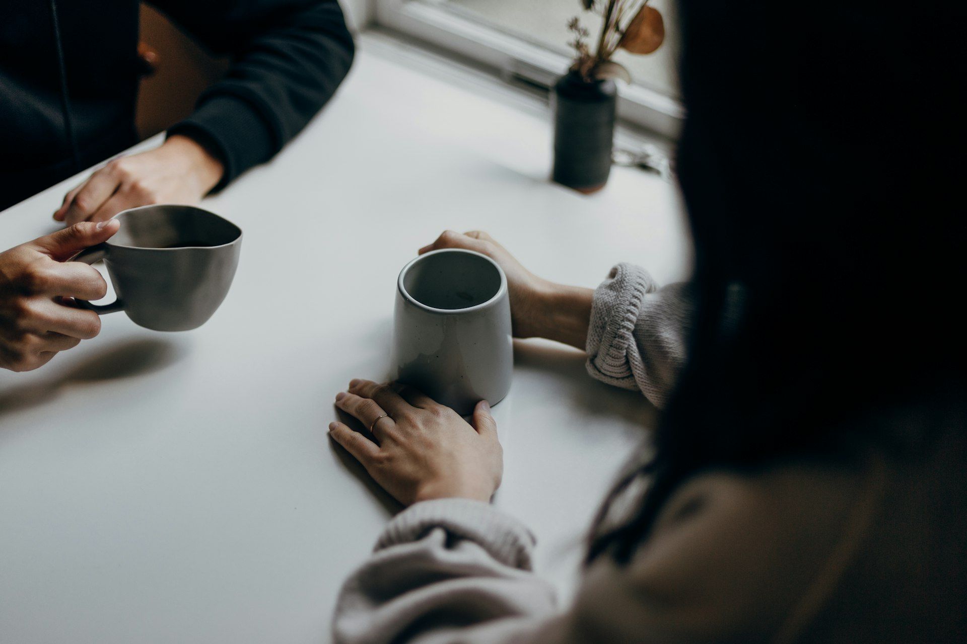 Two people's hands around coffee mugs on a white table