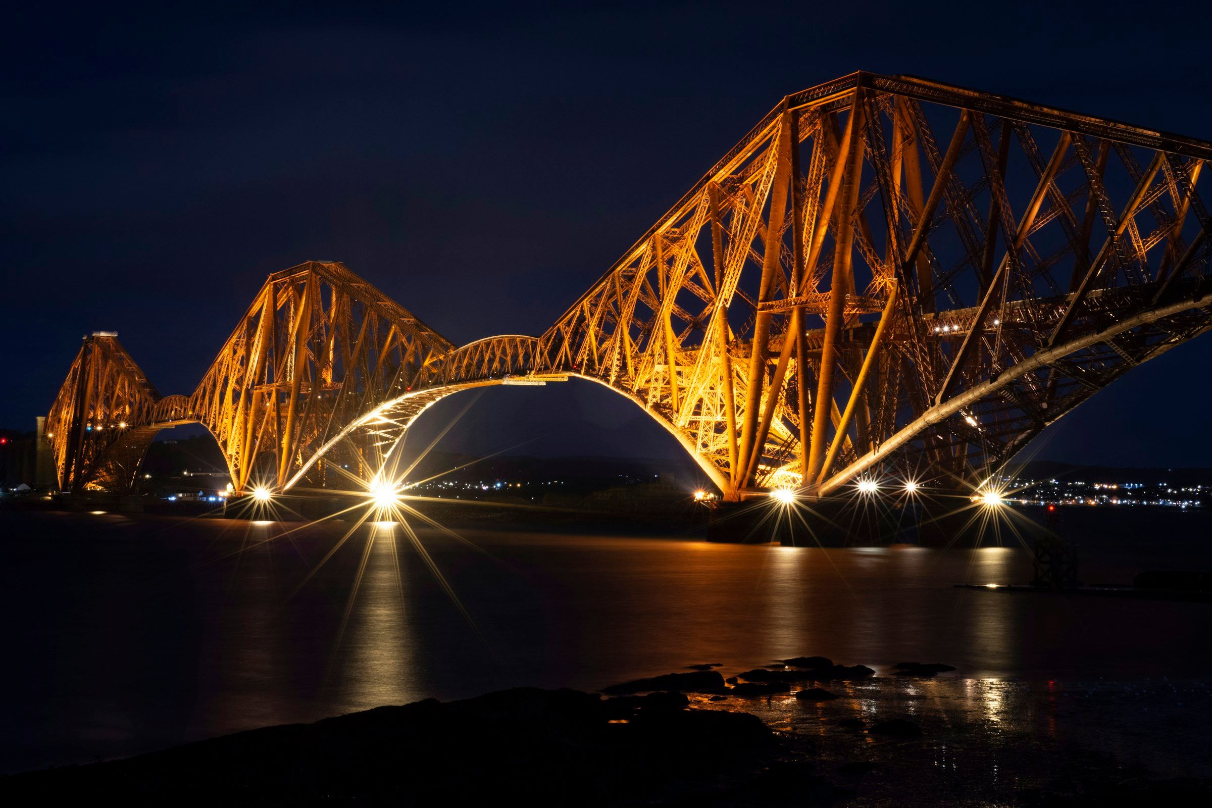 The Forth Bridge in Scotland lit up at night over the Firth of Forth
