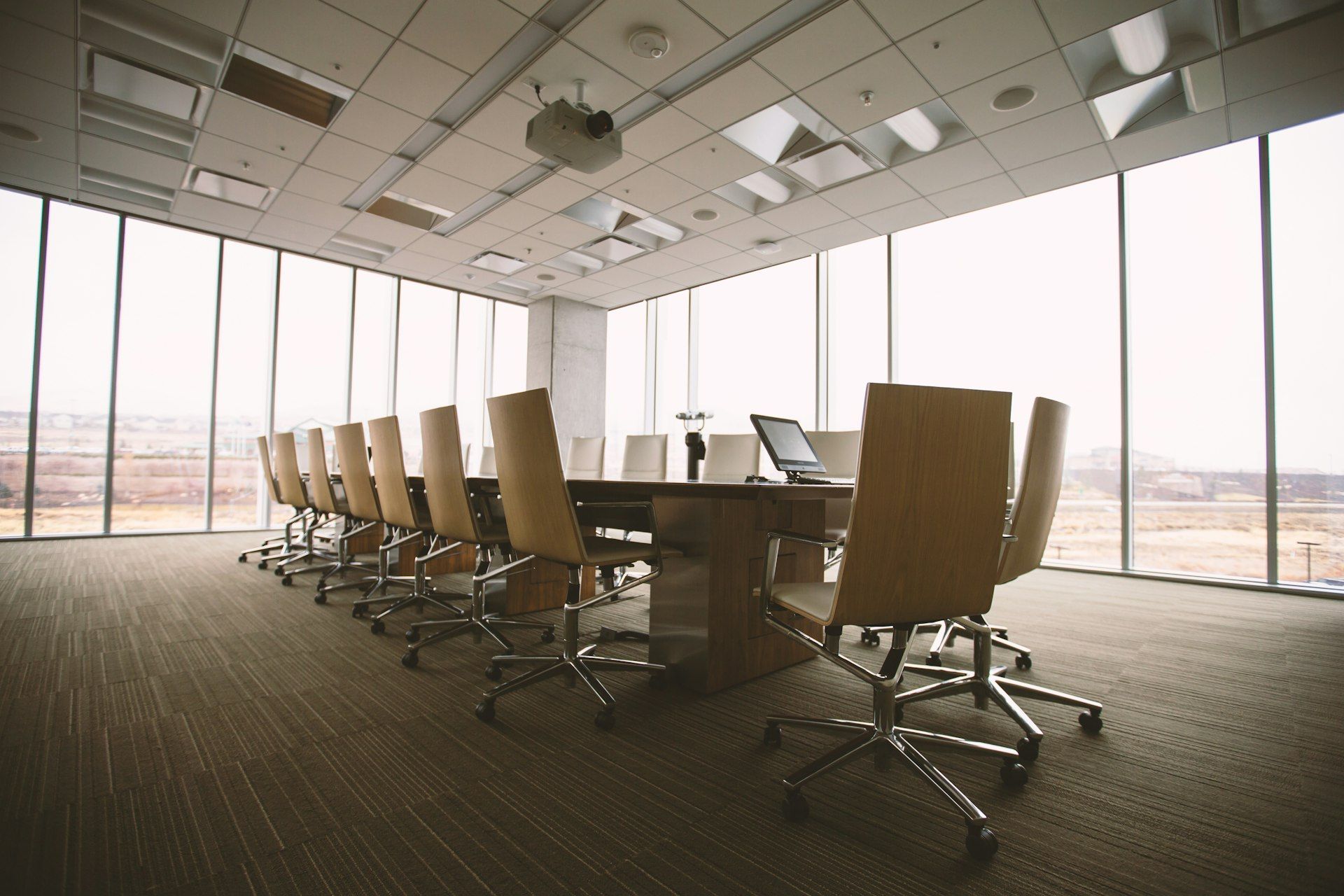 An empty boardroom with a long wooden table, leather chairs and floor-to-ceiling windows