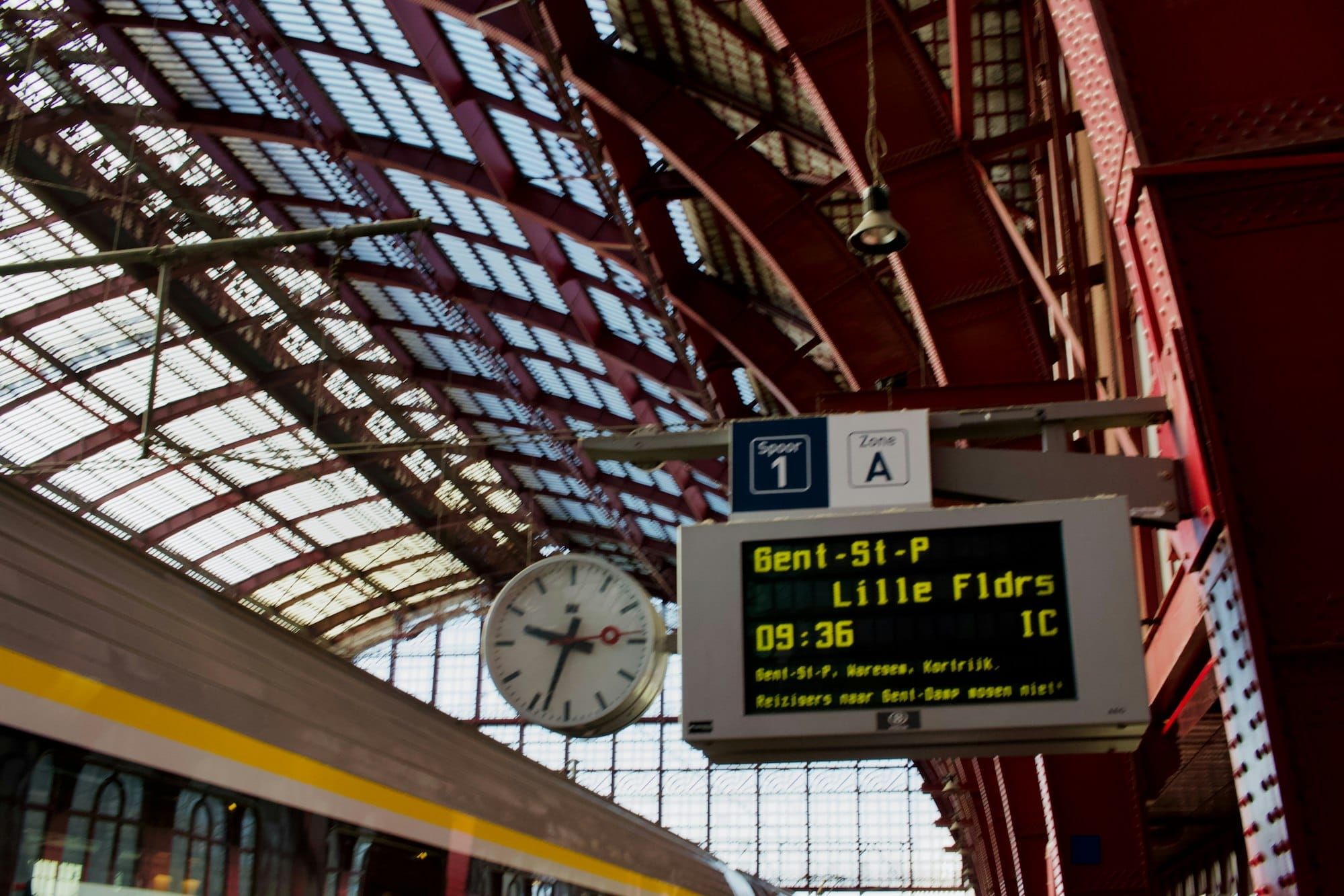 A departure board and clock under the glass roof of a European railway station