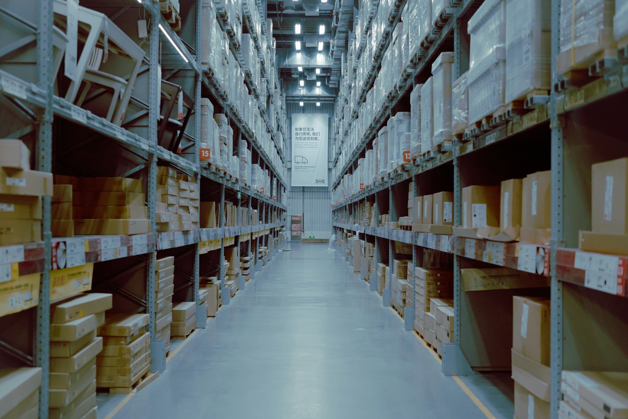 A long aisle of high warehouse shelves stacked with boxed goods