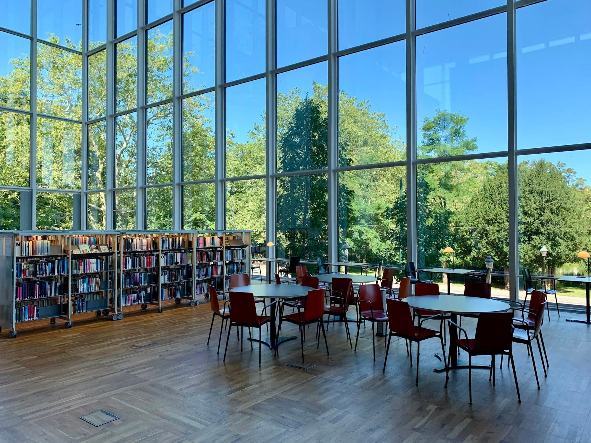 A bright library with tall windows, bookshelves and round reading tables