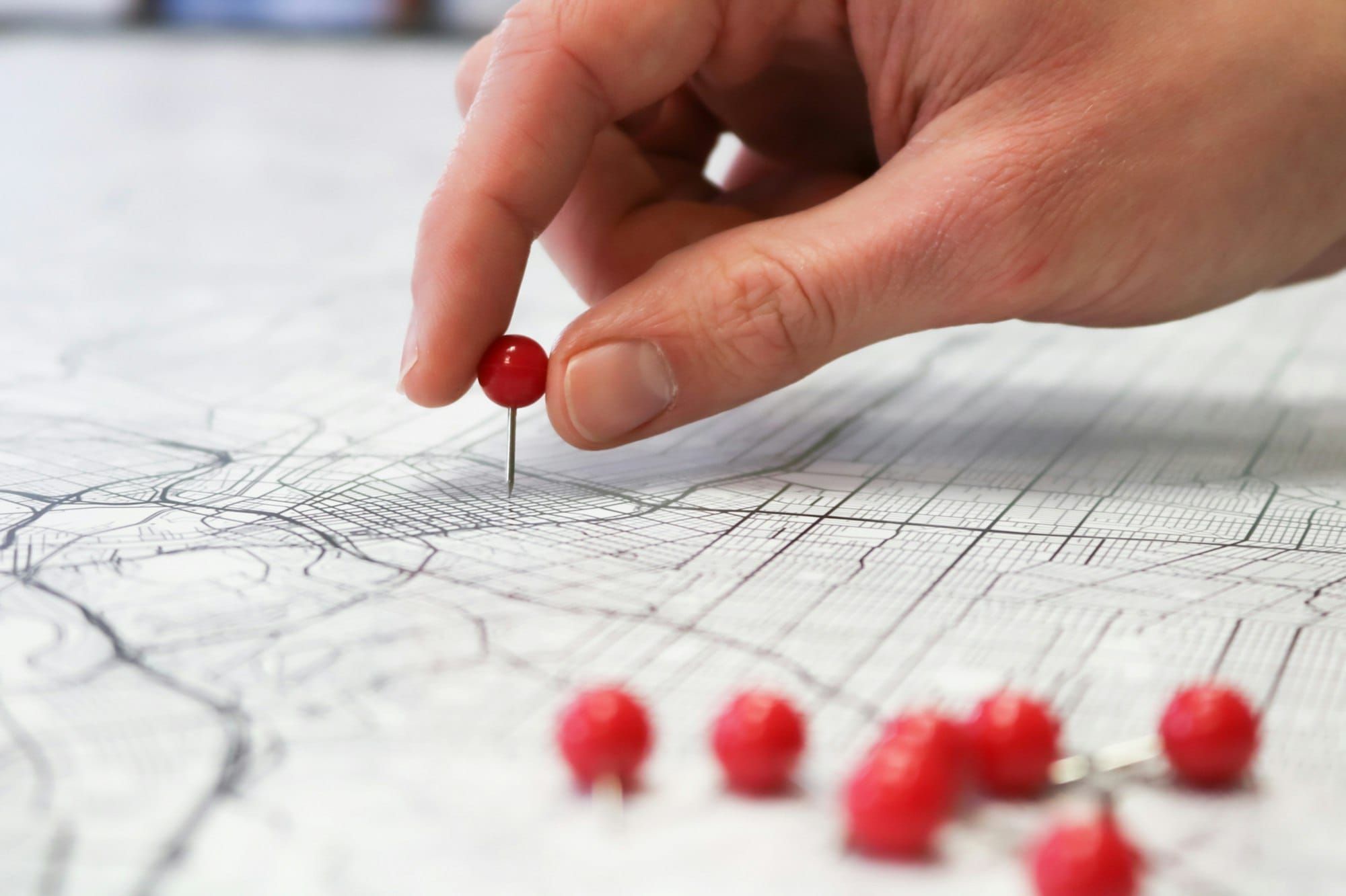 A hand placing a red pin on a printed city map