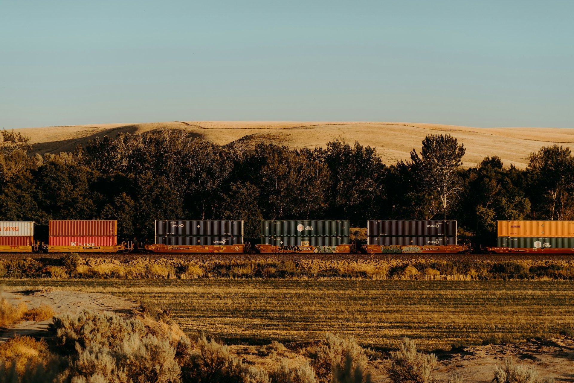 A container freight train crossing dry open country in low evening light