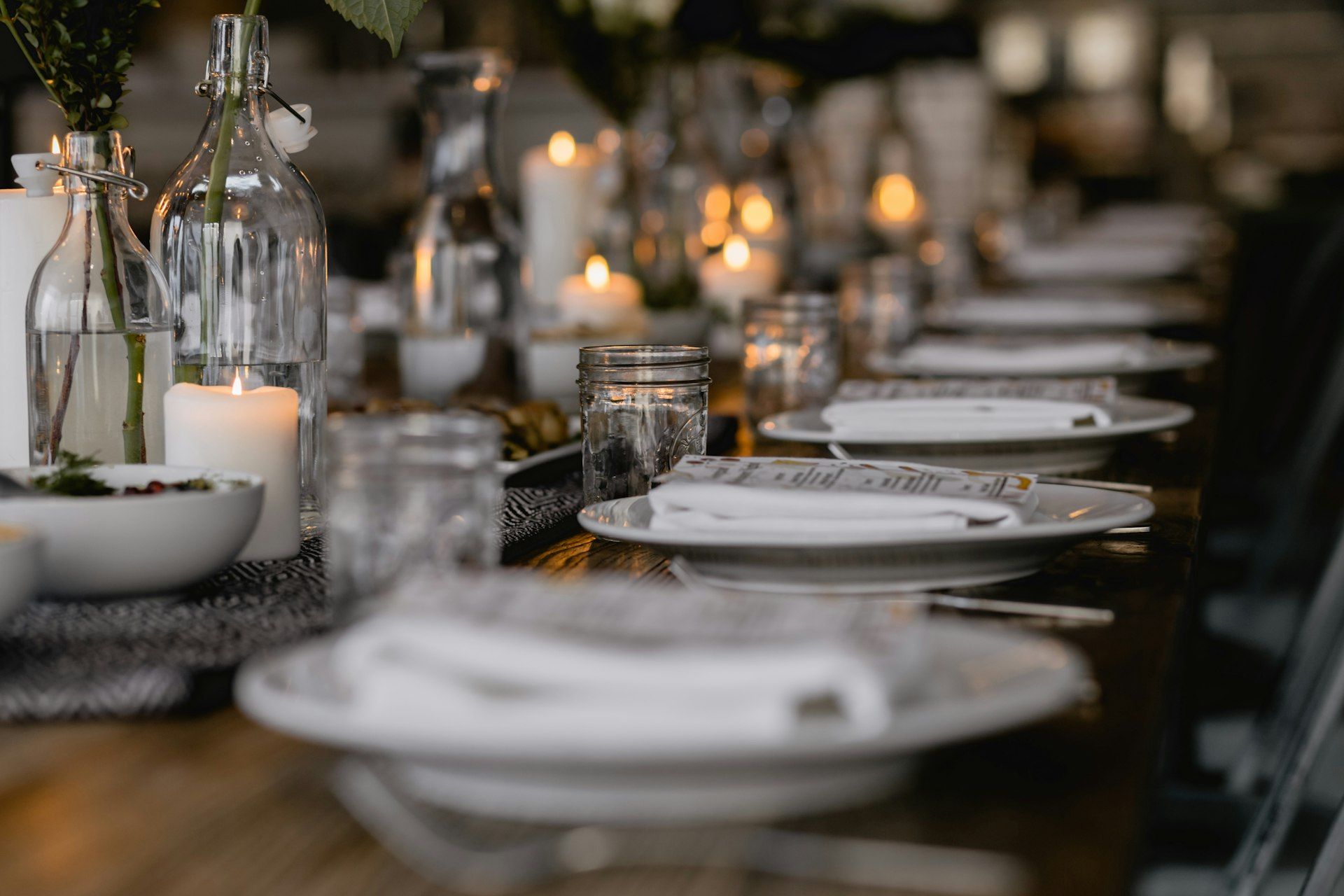A long dinner table set with white plates, glasses and lit candles