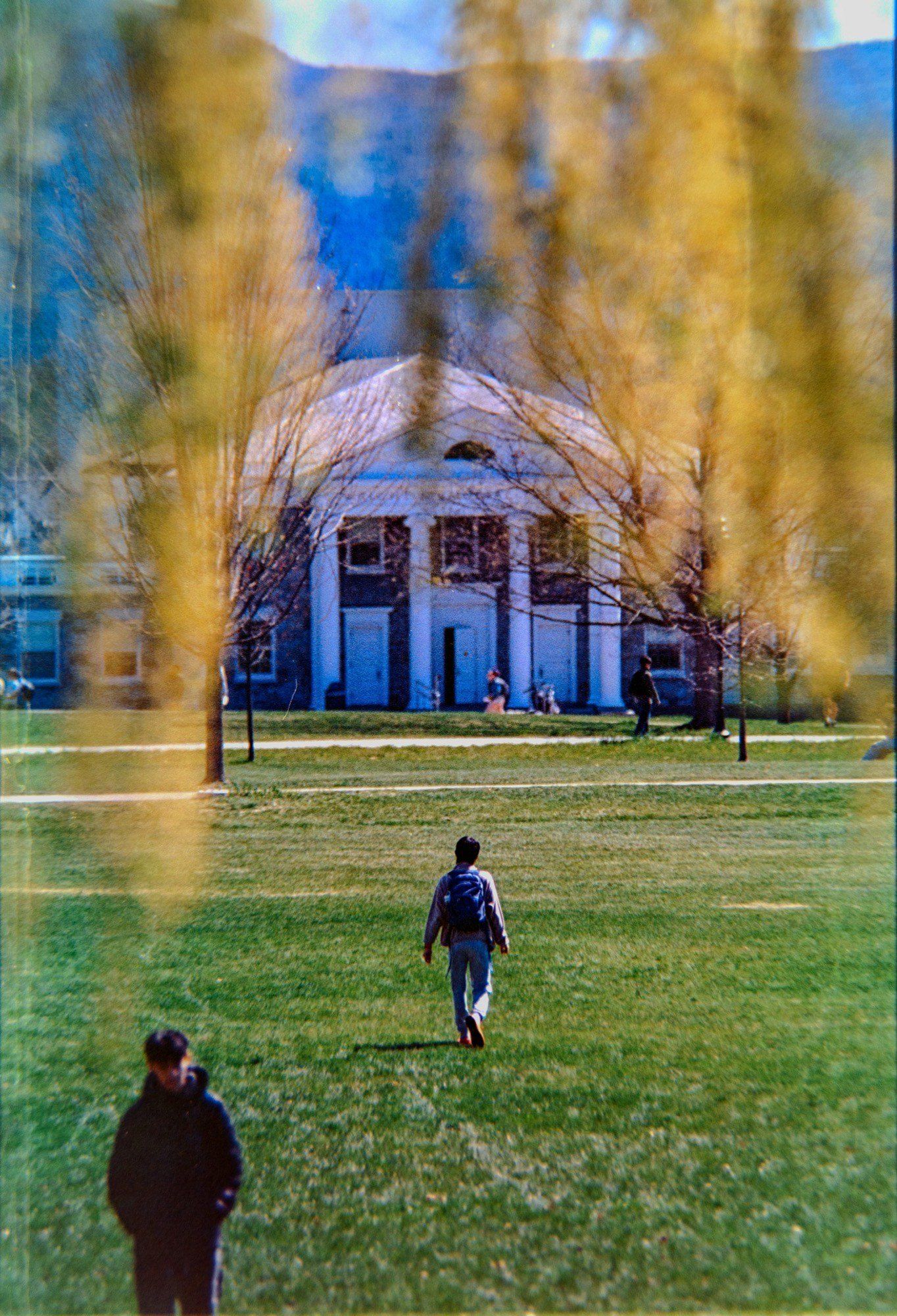 A student with a backpack walking across a university lawn towards a columned building